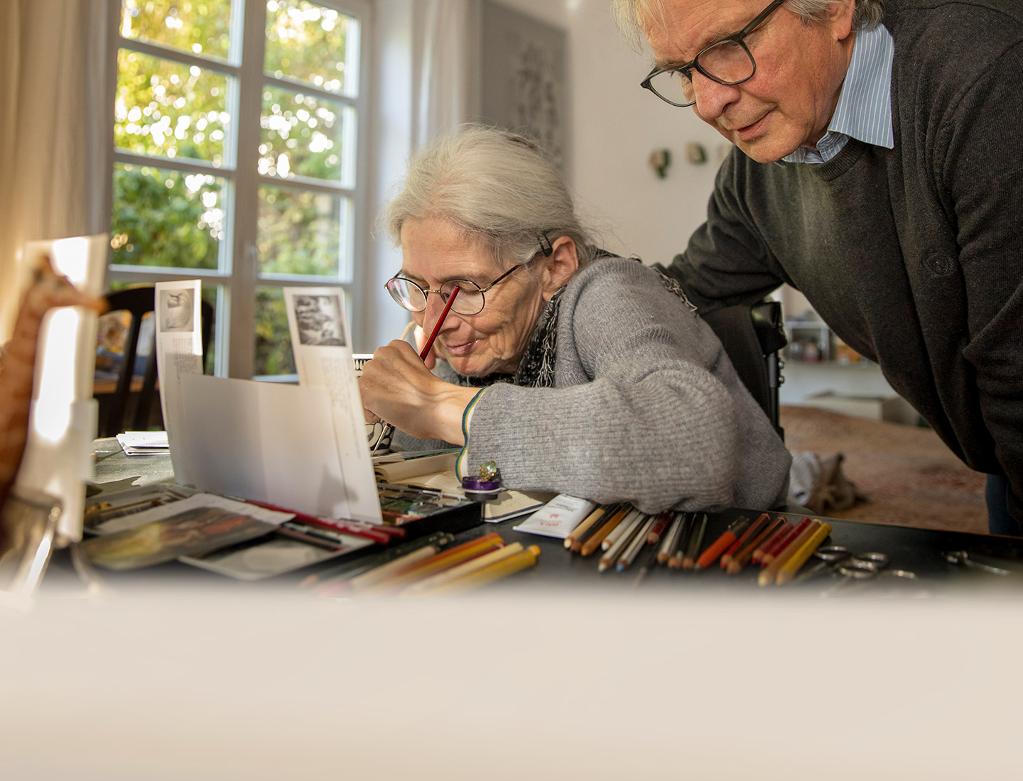 Family manager Heinrich looking over his wife’s shoulder while she paints