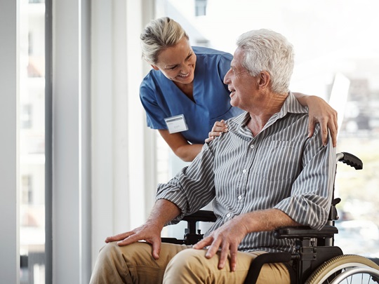Nursing home caregiver and resident in a wheelchair talking in a friendly environment.