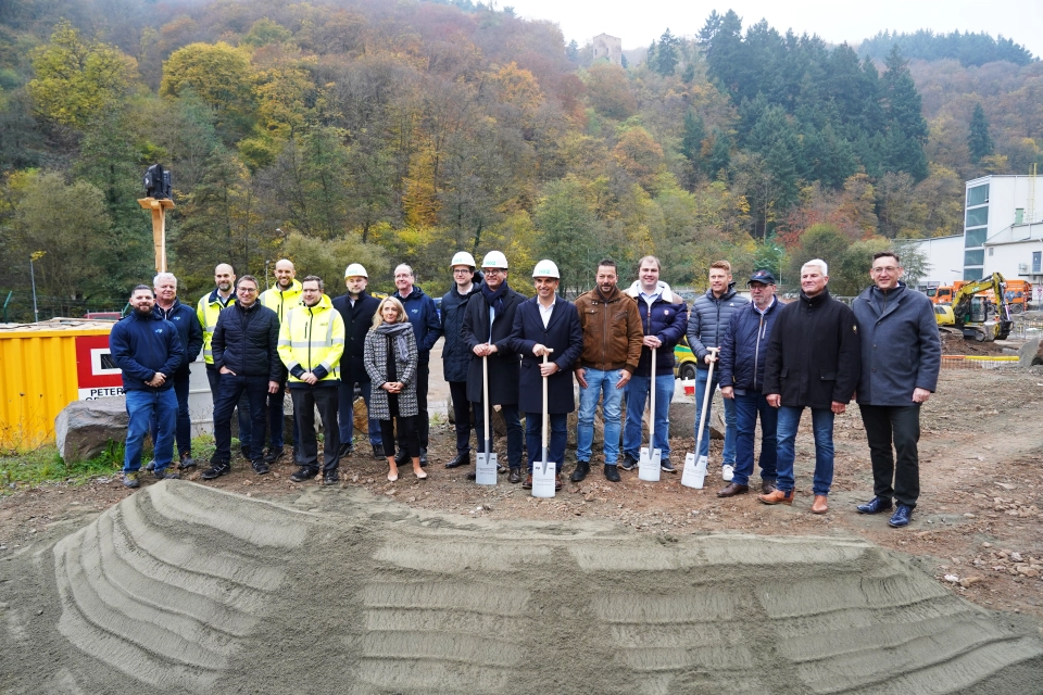  Group of people with shovels at a construction site, surrounded by autumn trees, breaking ground for a new project in a forest area.