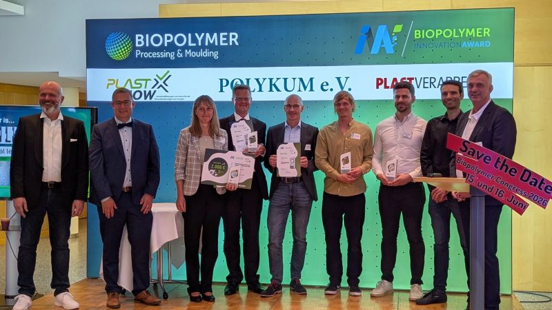 Group of award recipients holding certificates on stage at the Biopolymer Innovation Award, featuring banners from sponsors and officials, celebrating achievements.