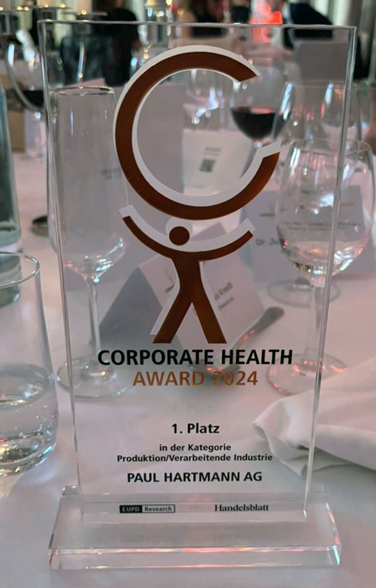 Corporate Health Award 2024 trophy displayed on a dining table setting, awarded to Paul Hartmann AG for excellence in the production and processing industry.