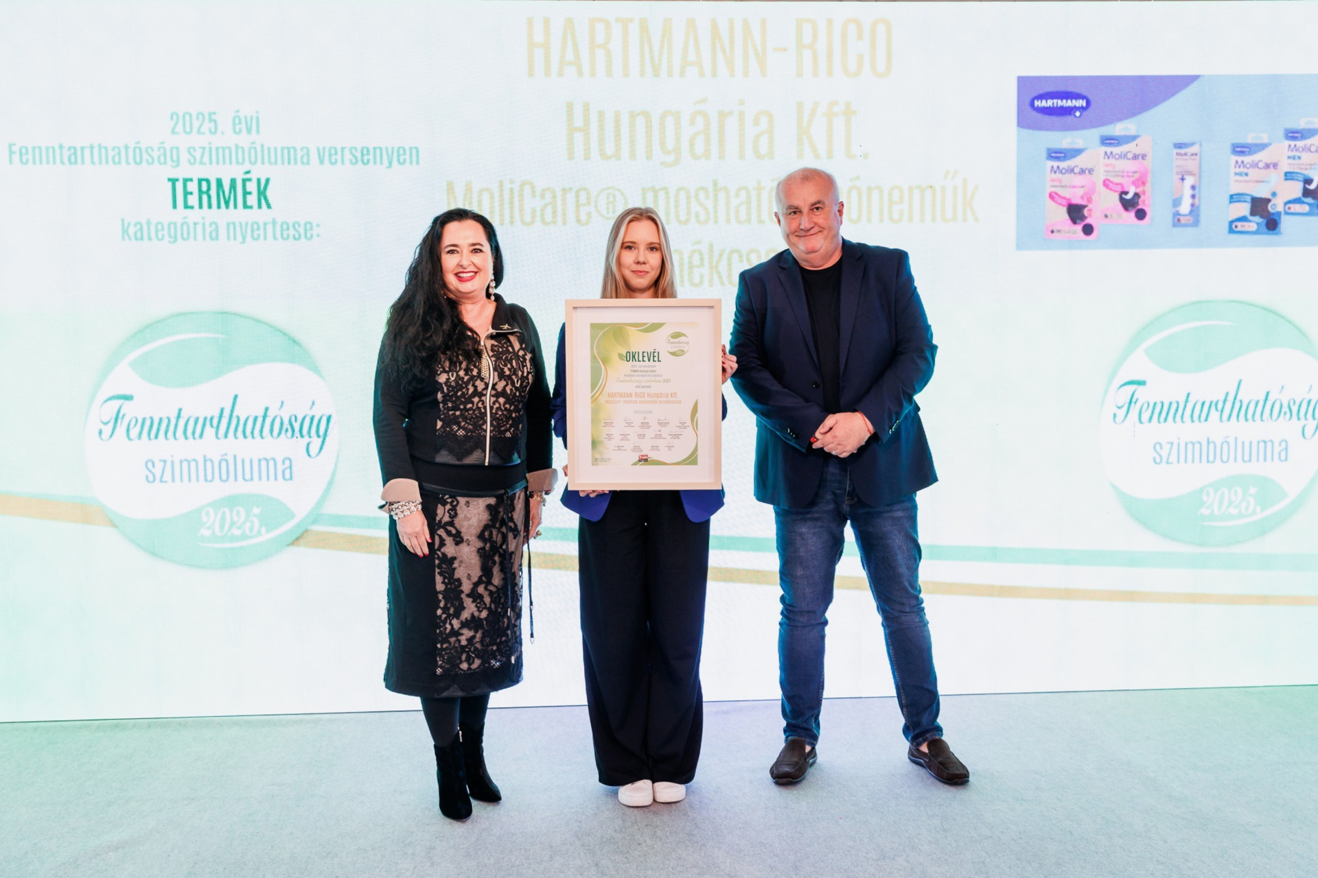  Three people stand on stage with an award for MoliCare incontinence products, with product images displayed in the background.