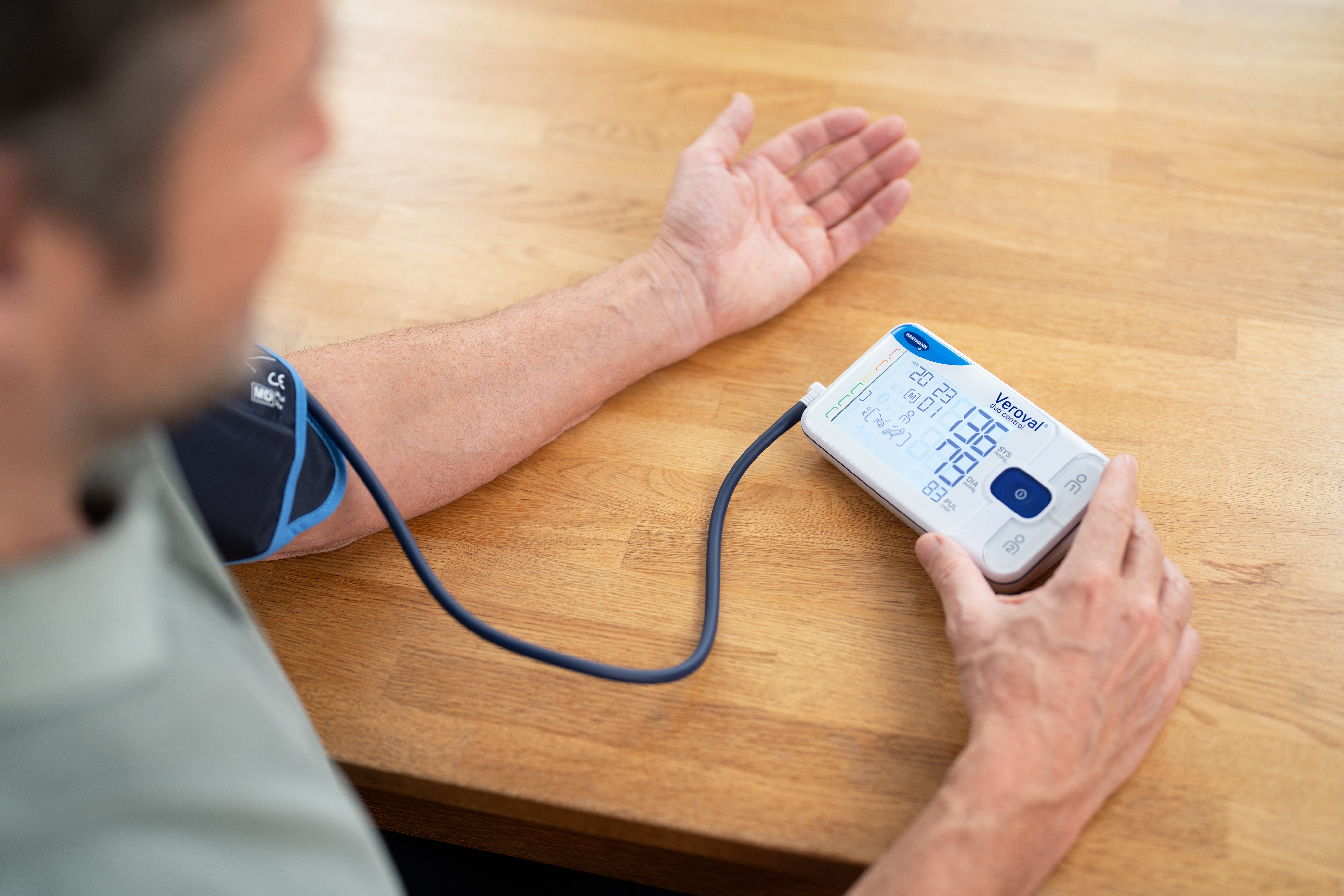  A person using a digital blood pressure monitor on their arm, showing a clear display of blood pressure readings for home healthcare use.